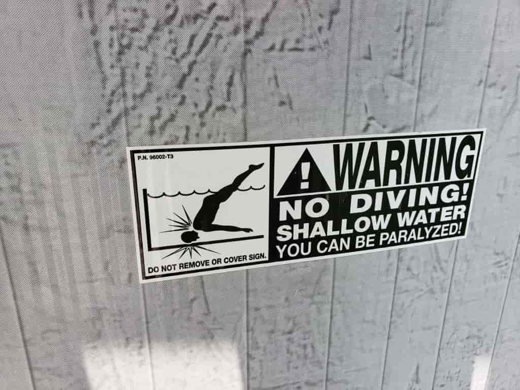 No diving shallow sign displayed on the outside of a metal swimming pool.