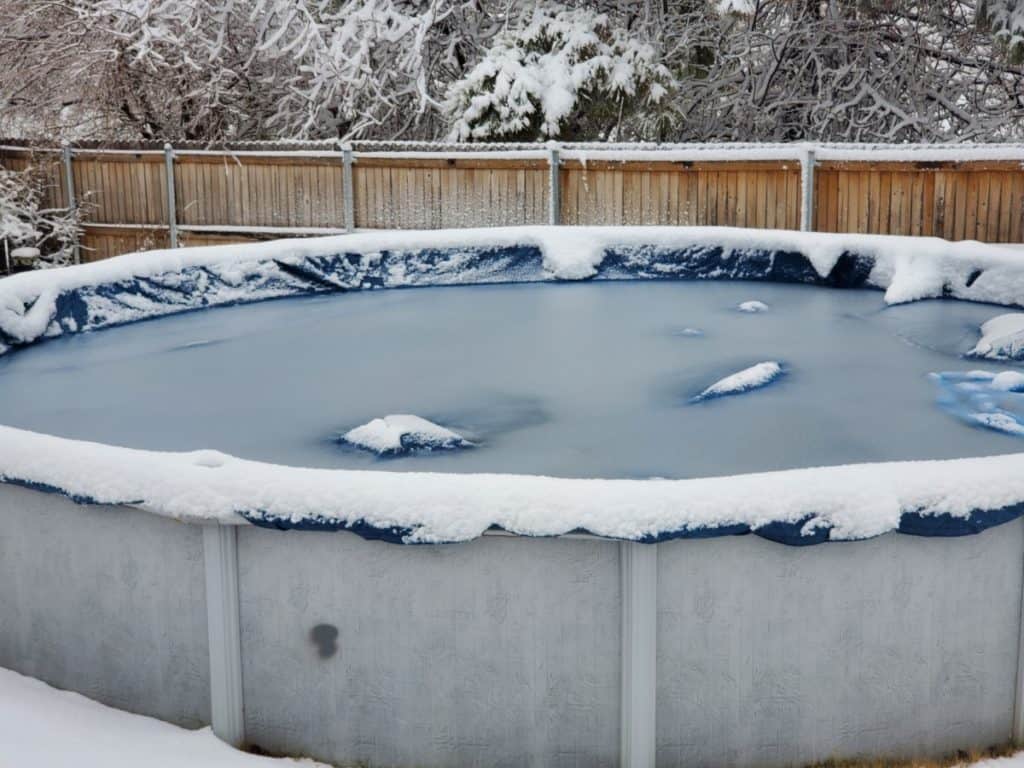 An above ground pool with snow around the edges and the covered center of it frozen with ice.